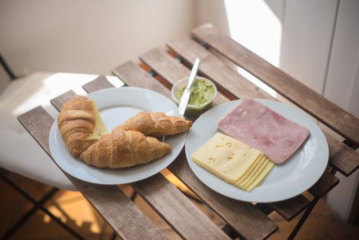 Delicious Portuguese breakfast with croissants, cheese, ham, and guacamole on a rustic wooden table.