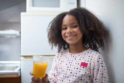 Photo of a Kid Smiling While Holding a Glass of Orange Juice