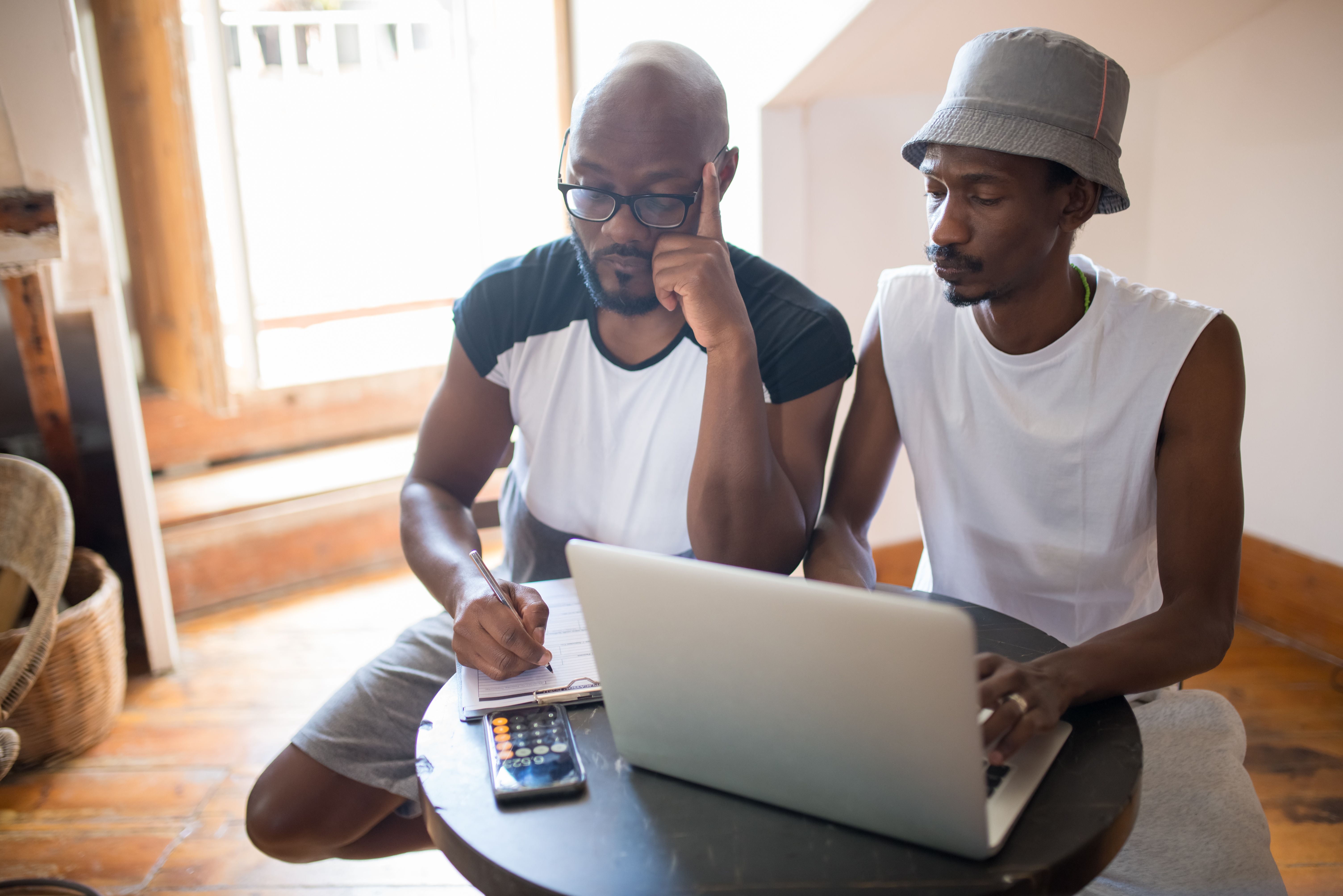Two men collaborating indoors with a laptop and clipboard, showcasing teamwork and focus.