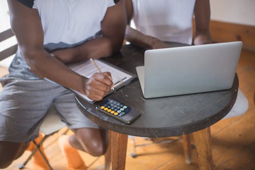 Two People in White T-shirts Using Laptop and Calculator