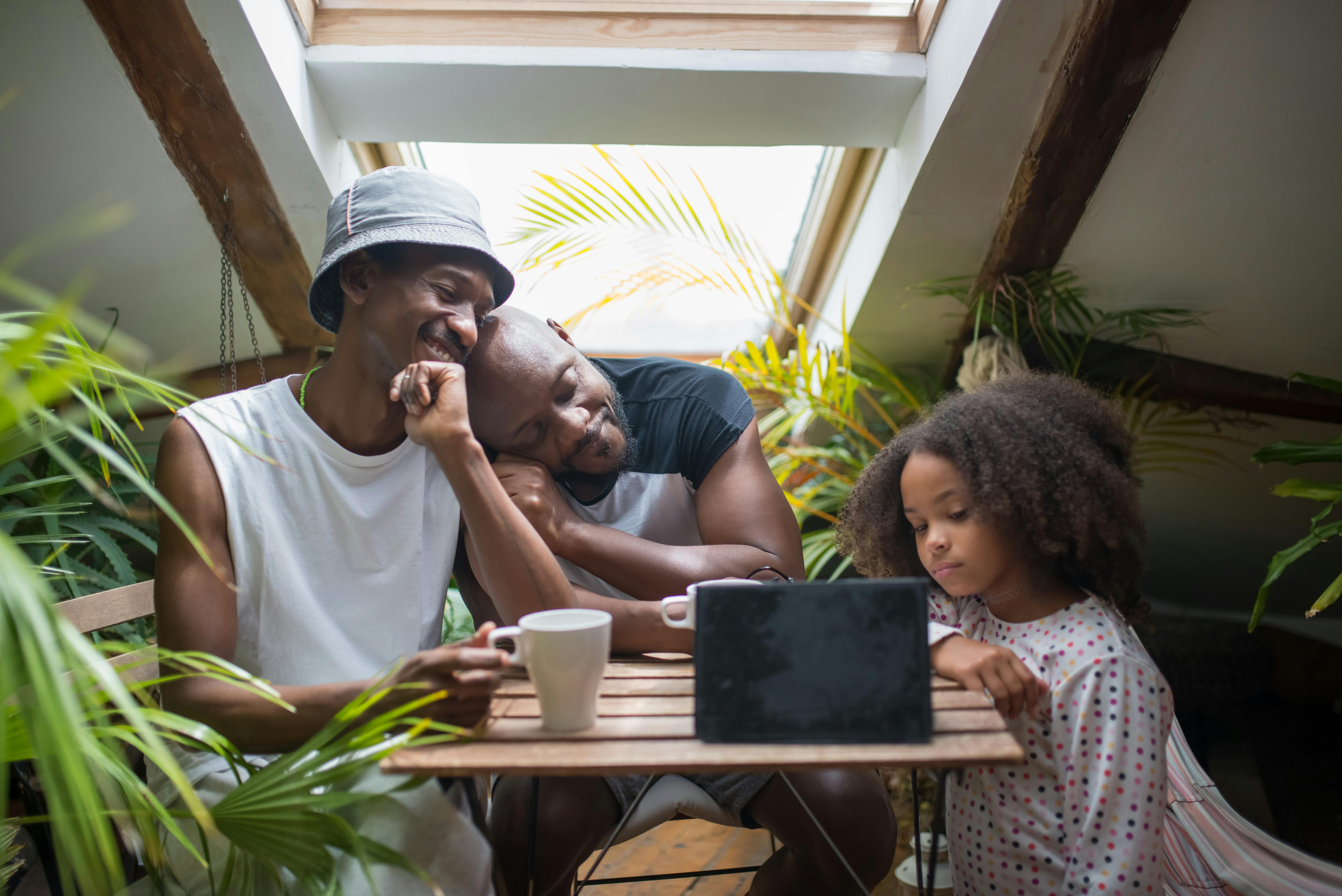 a same sex couple looking at their daughter looking at the tablet on a wooden table