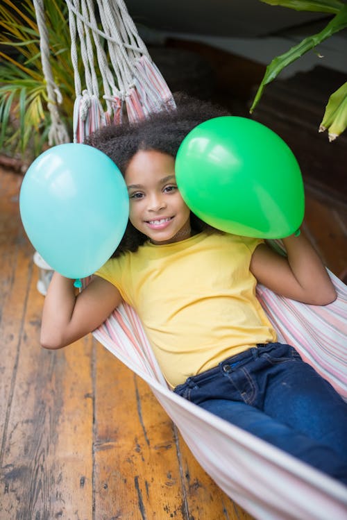 Girl Lying on a Hammock Holding Green and Blue Balloons