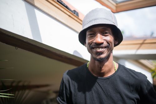 Free A cheerful man wearing a black shirt and bucket hat, smiling brightly indoors. Stock Photo