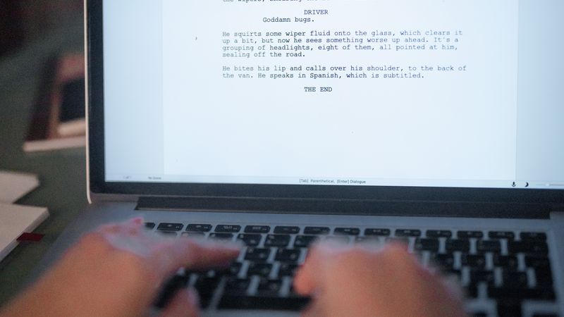 A close-up shot of hands typing a film script on a laptop, focusing on creativity and screenplay writing.