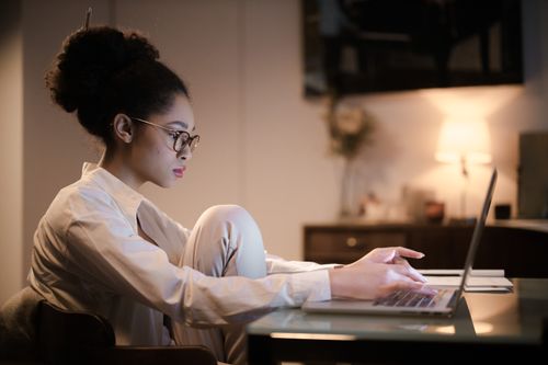 Free Focused woman typing on a laptop at home, creating a warm indoor study ambiance. Stock Photo