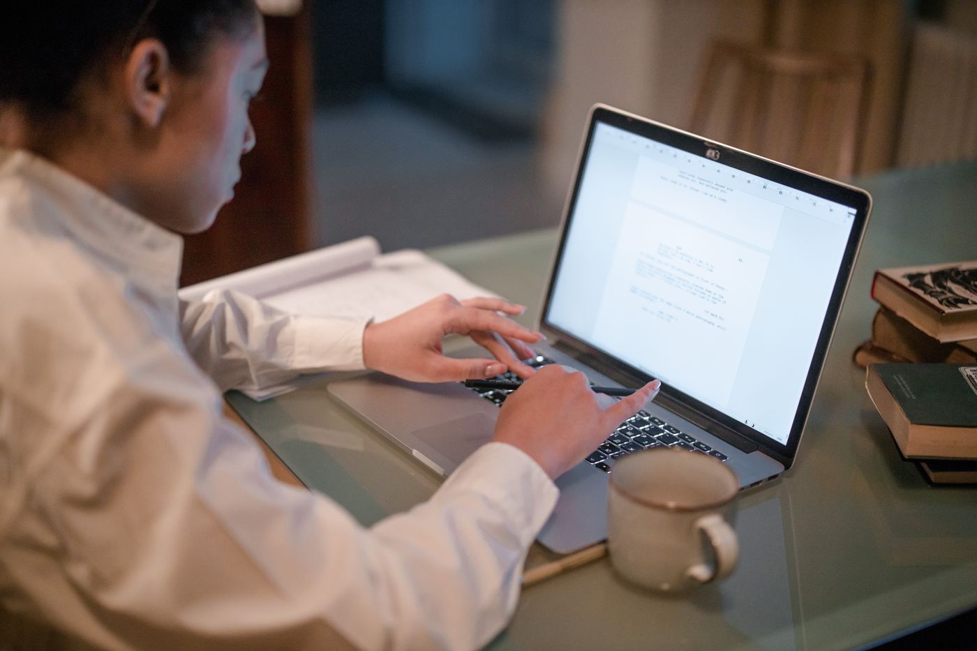 Woman typing a long text document on a laptop beside a coffee mug and books