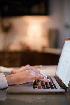 Close-up of hands typing on a laptop, working indoors with a blurred background.