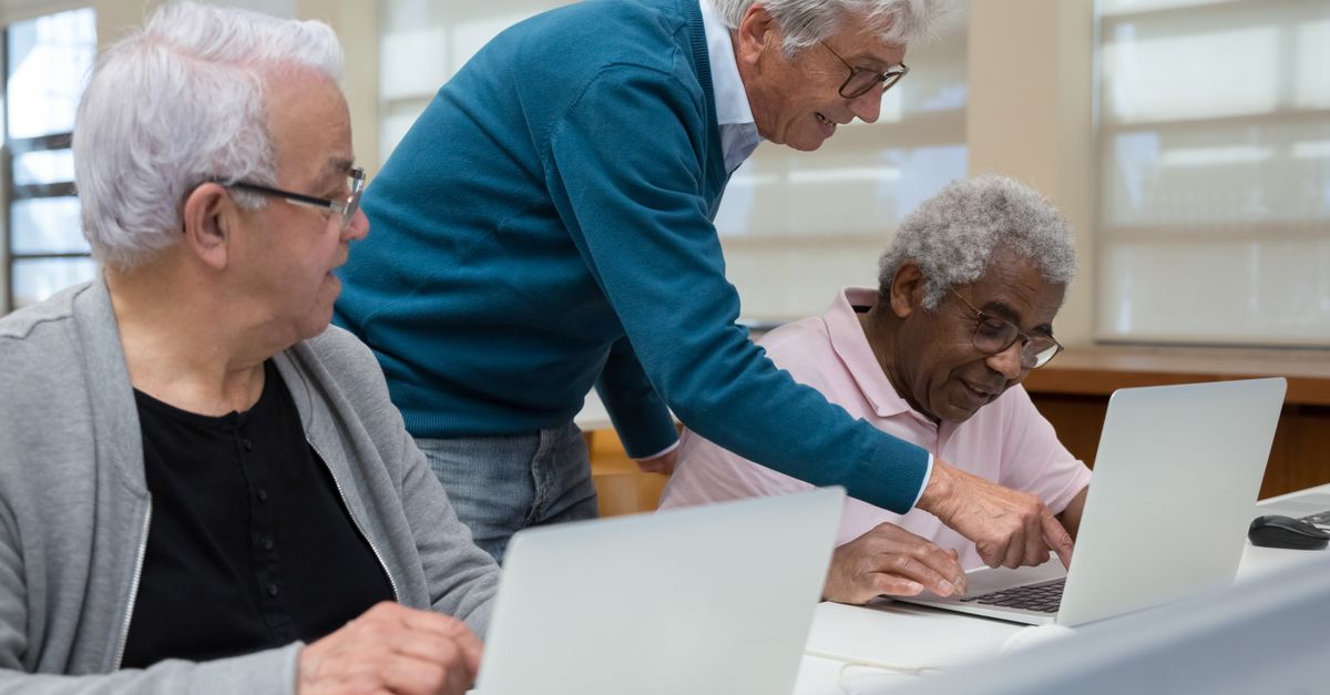 Three senior adults collaborating in a classroom setting on laptops, focusing on technology learning, illustrating Older Americans Act Services for Seniors โ 1-800-MEDIGAP, America's Trusted Toll-Free Number.