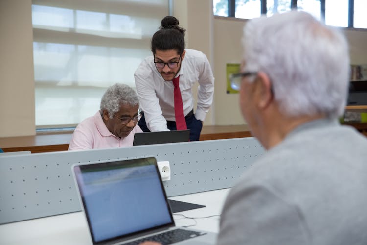 Man In White Shirt Teaching Elderly To Use Laptop