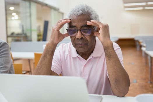 Elderly man deeply focused on laptop work in a modern library setting.