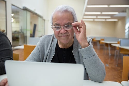 Elderly Man Sitting at the Desk and Using a Laptop 