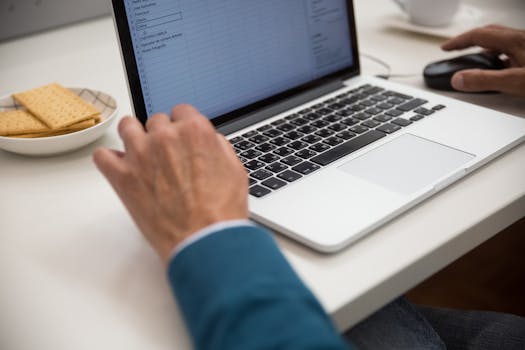 A person working on a laptop at a desk with snacks, emphasizing productivity and technology.