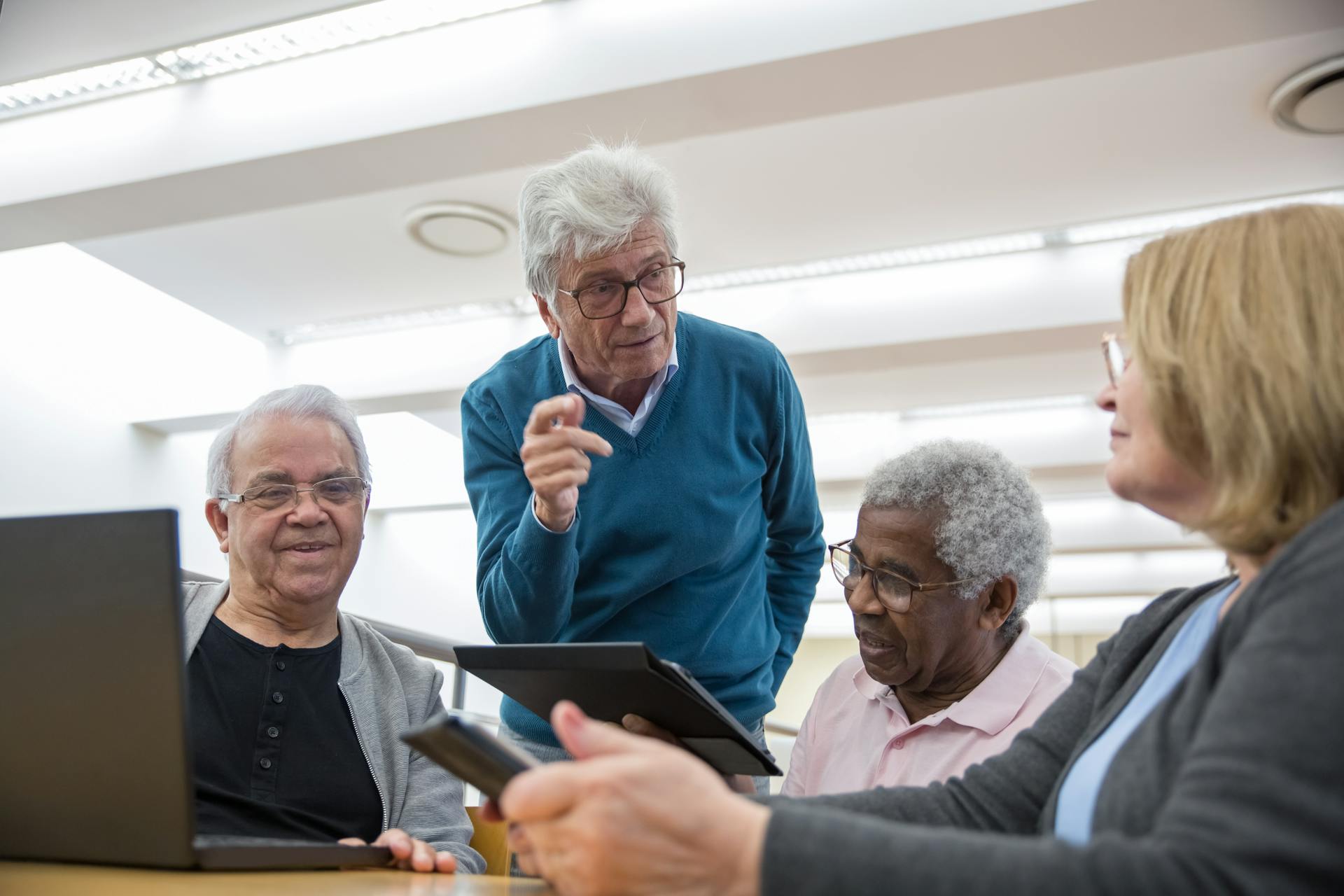 Elderly group engages in digital discussion with tablets and laptops.