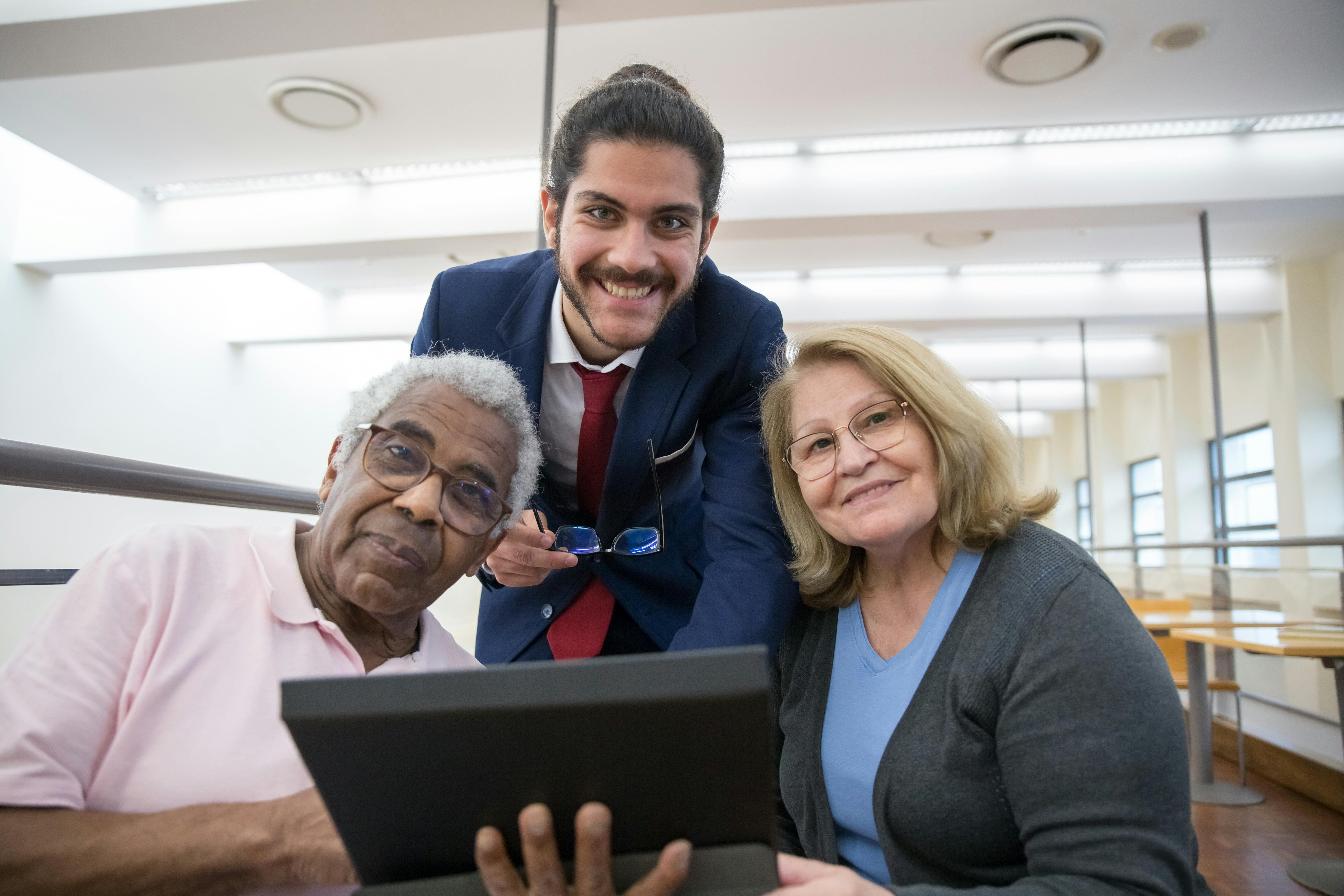 Free Seniors engaging with technology under the guidance of a young professional in a library. Stock Photo