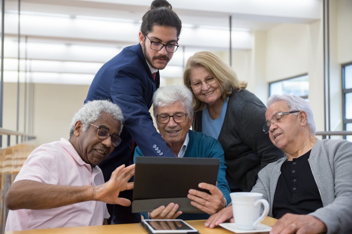 Free Group of seniors and a young man collaborating using a tablet during a meeting indoors. Stock Photo