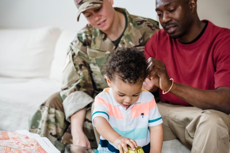 Woman In A Military Uniform And Father Playing With Her Baby Son 