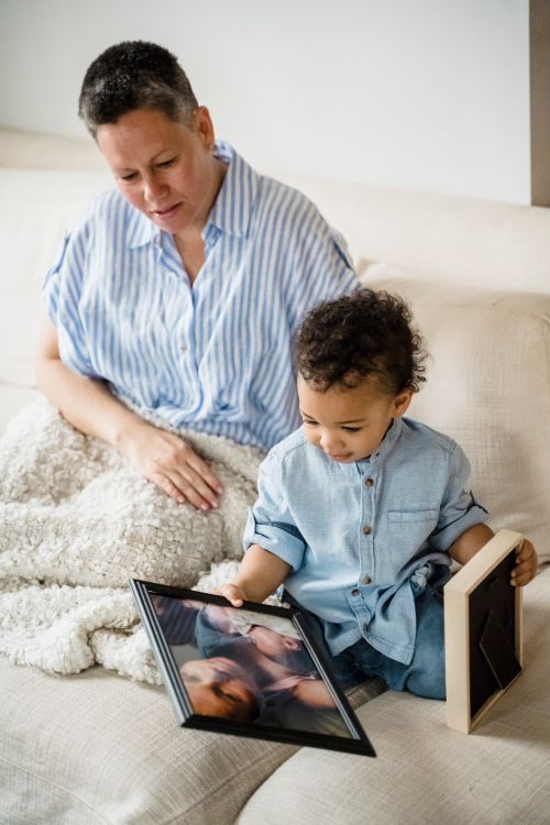 Free A mother and her young son sitting on a sofa, looking at family photos together in a cozy living room. Stock Photo