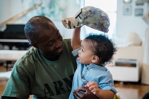 Free Baby Boy Holding a Camouflage Cap of Man in Green Army Shirt Stock Photo