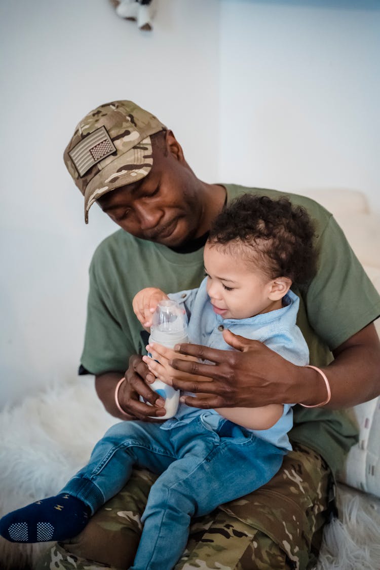 Soldier Dad With His Baby Son Sitting On His Lap With A Milk Bottle