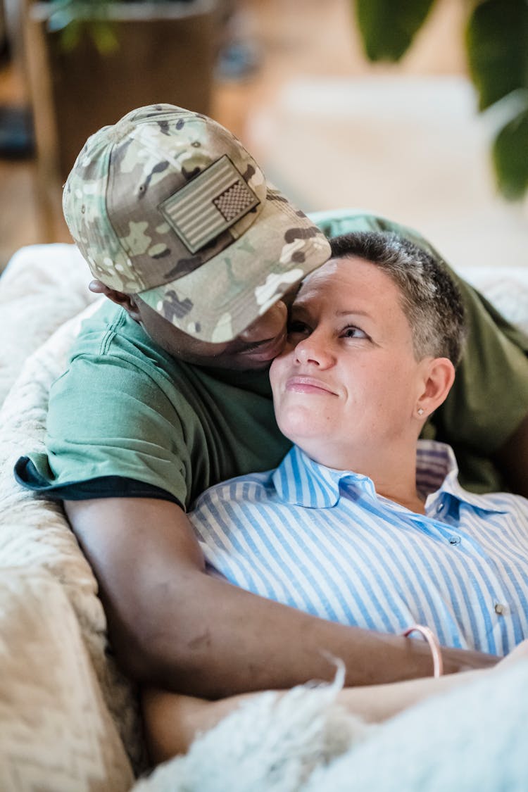 Man In Military Uniform Sitting On A Sofa And Embracing His Wife 