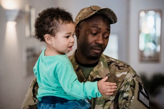 Tender moment between military father and son indoors in loving embrace.