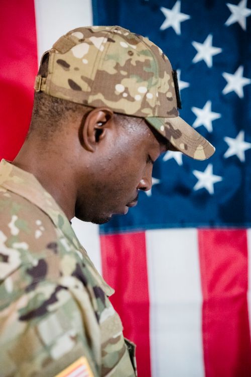 Free Side view of a soldier in uniform with US flag background, symbolizing patriotism. Stock Photo