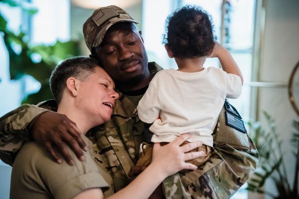 Service member in uniform hugging spouse and young child at home before a military PCS move