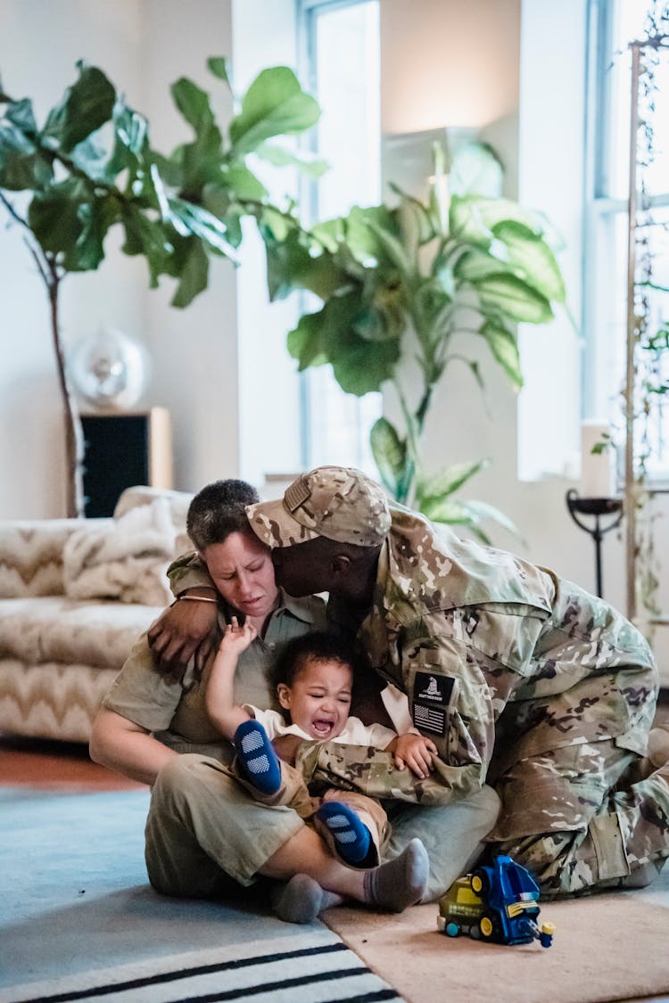 Man In Military Uniform Giving A Goodbye Hug And Kiss To Woman And A Crying Boy