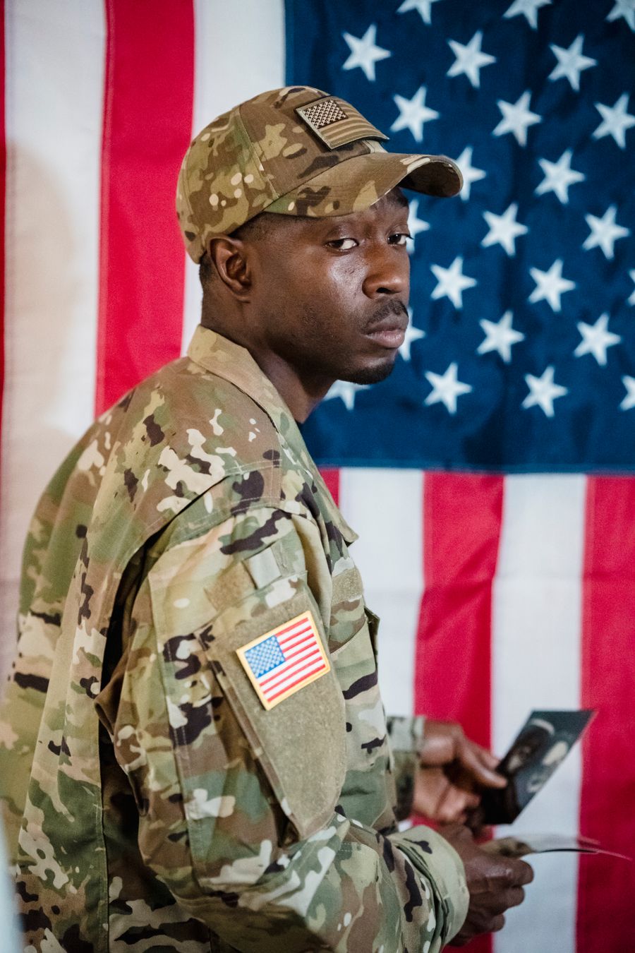 Soldier in uniform standing with an American flag backdrop, holding a photograph