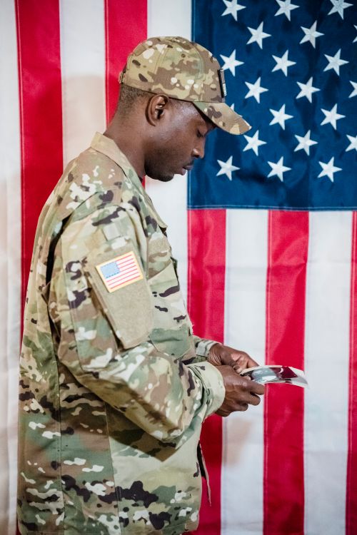 Free American soldier in camouflage uniform reading a document in front of the US flag. Stock Photo