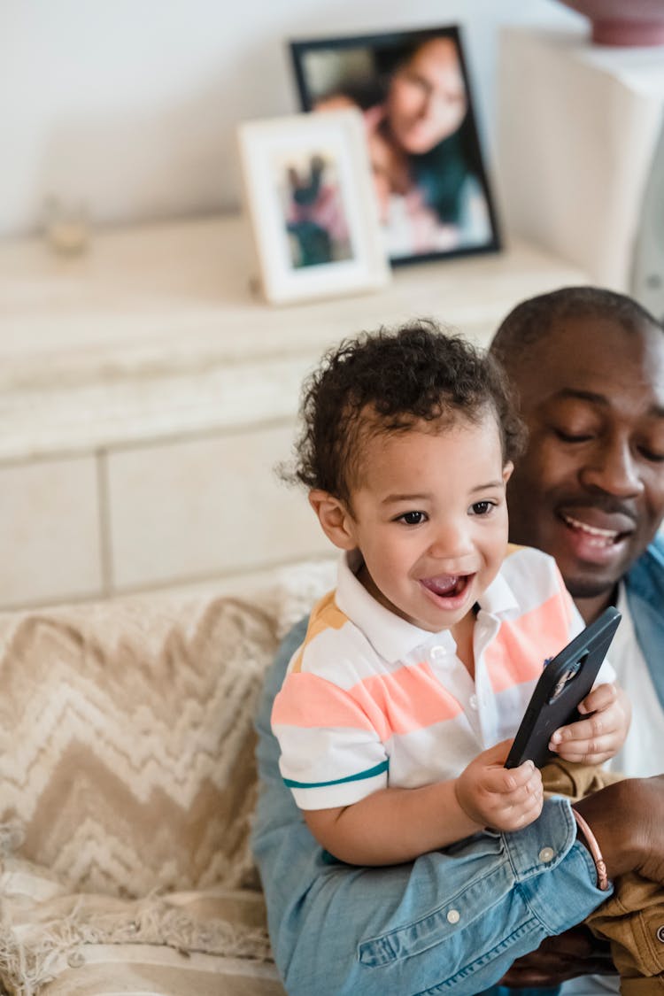 Laughing Boy Playing A Game On A Phone With His Father