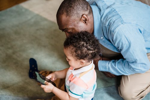 A Child using a Smartphone next to his Father