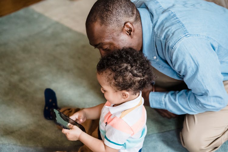 A Child Using A Smartphone Next To His Father