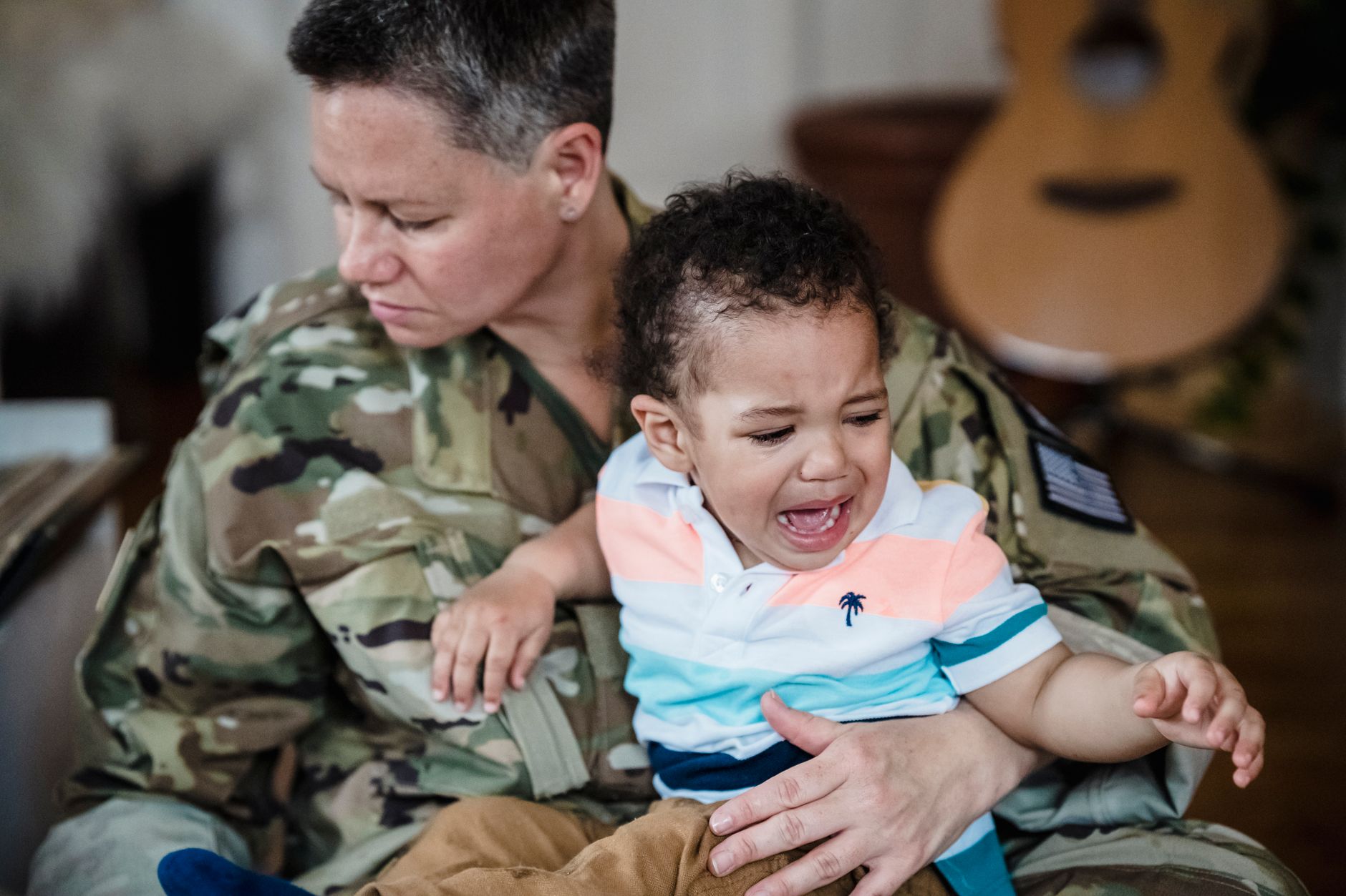 A soldier in uniform comforts a crying child, depicting the emotional bond and sacrifice of military families.