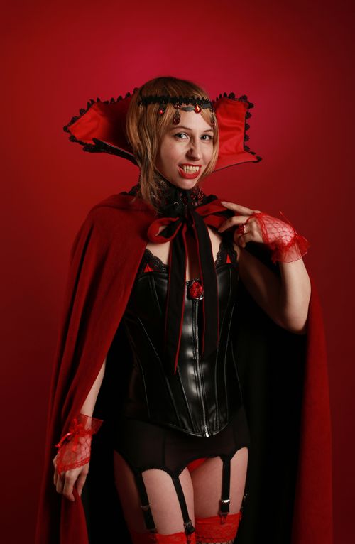 Free A woman in a gothic vampire costume poses against a red studio background. Stock Photo