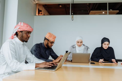 Free A multicultural team in traditional attire working on laptops in a contemporary office setting. Stock Photo