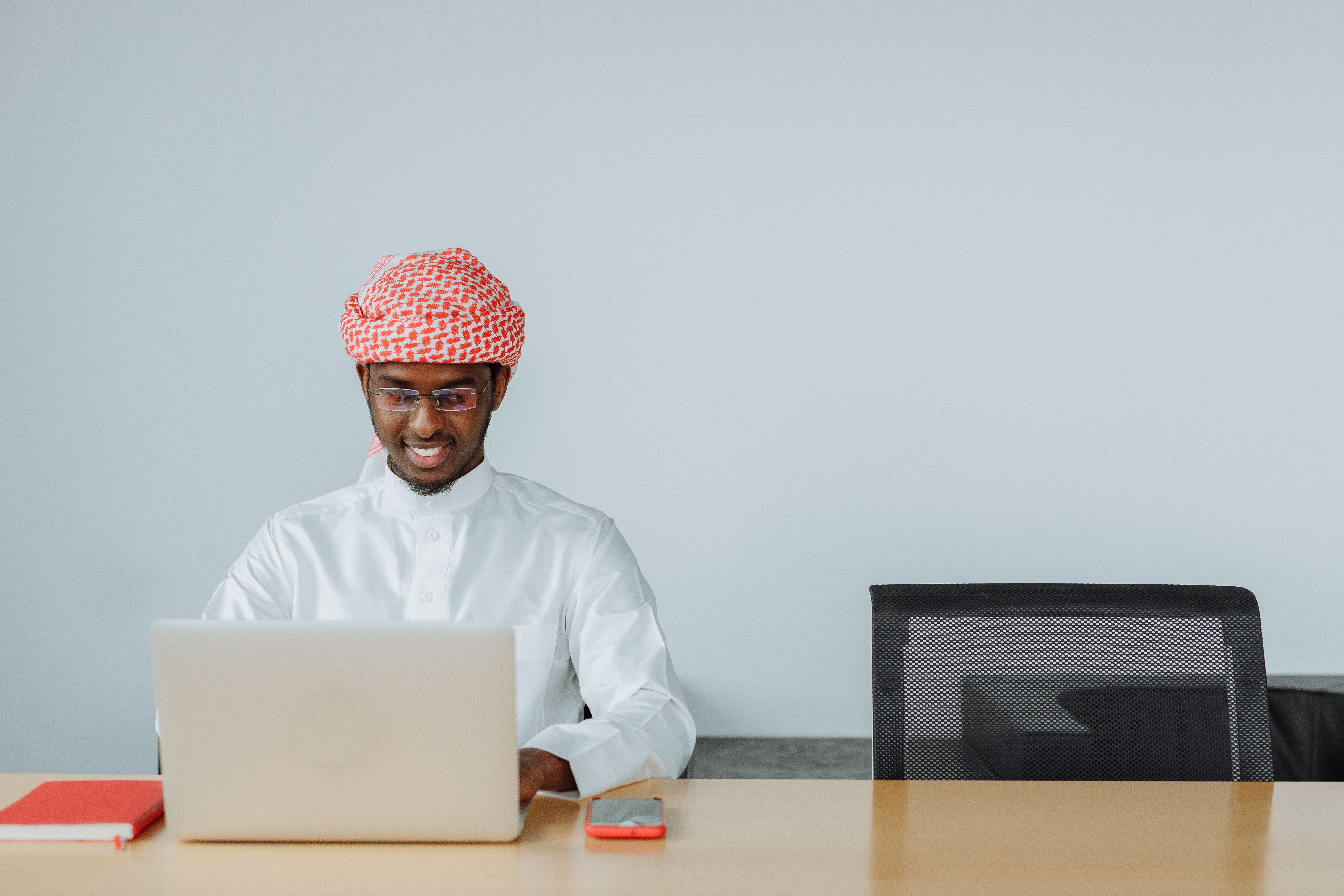 Man typing on a laptop at a wooden desk with notebook and coffee cup nearby in a home office environment