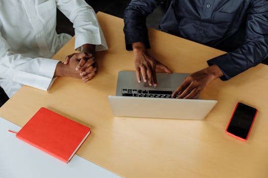 Two professionals collaborate using a laptop at a modern office desk. Meetings and productivity in one image.