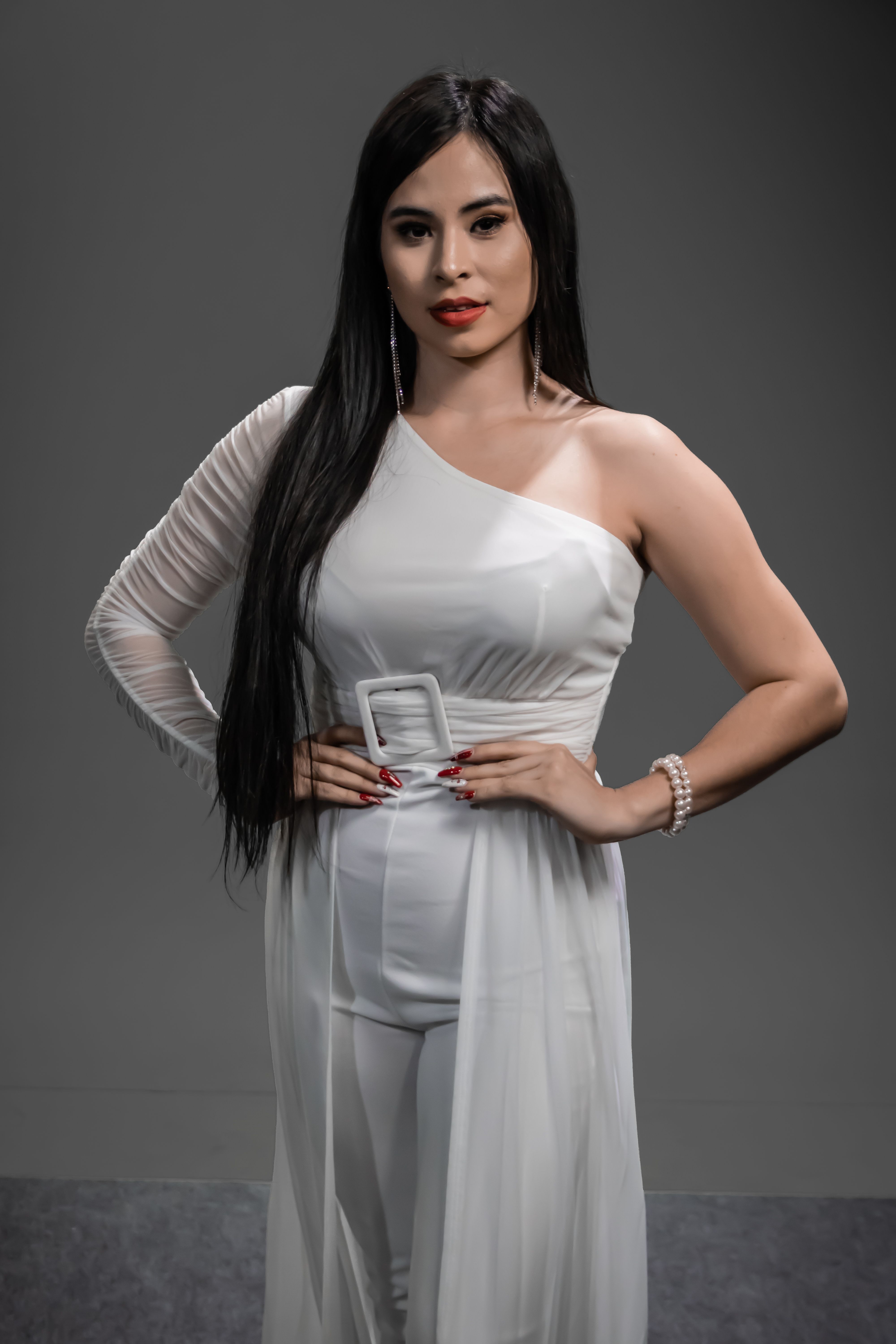 Stylish portrait of an elegant woman posing confidently in a white one-shoulder dress against a neutral studio background.