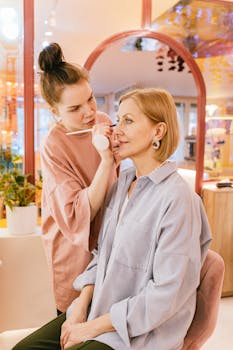 Makeup artist applying lipstick to mature woman in beauty studio with warm ambiance.