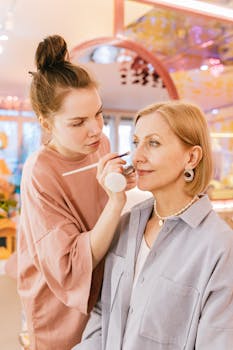 A makeup artist skillfully applies cosmetics to a mature woman in a salon setting.