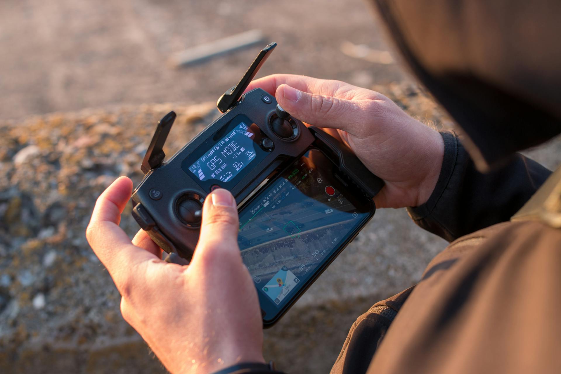 Close-up view of hands operating a drone controller outdoors at sunset.