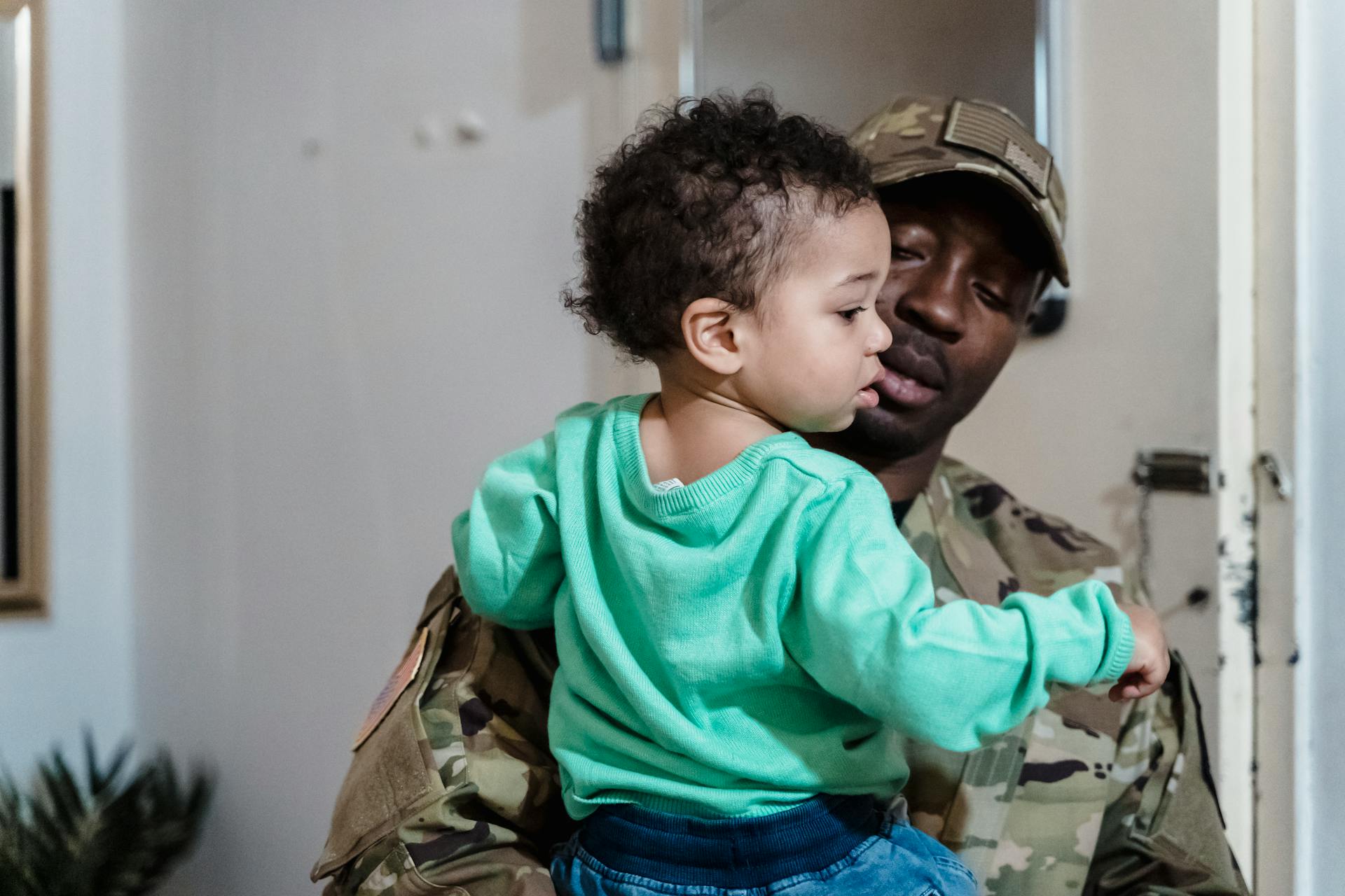 Man in Army Combat Uniform Carrying a Toddler