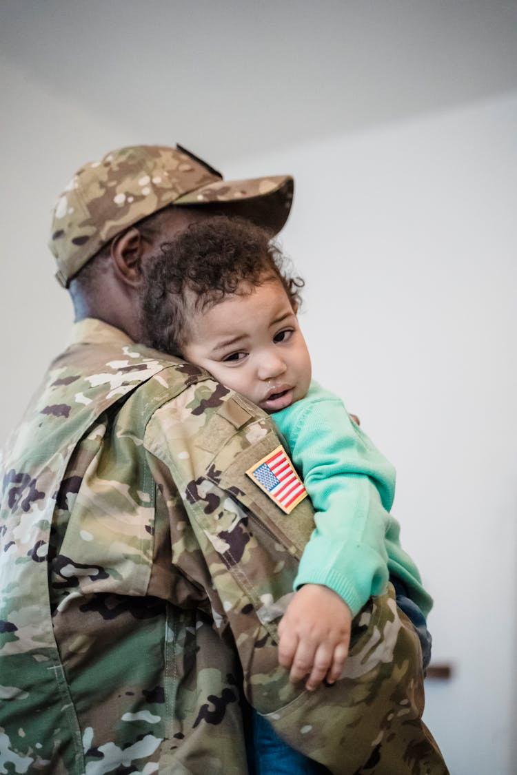 A Man In Military Uniform Carrying A Baby