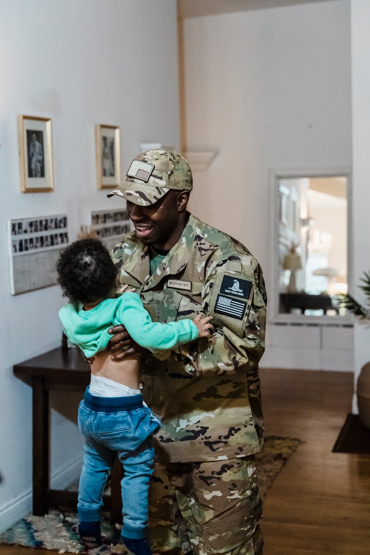 A Father In Military Uniform Carrying A Child