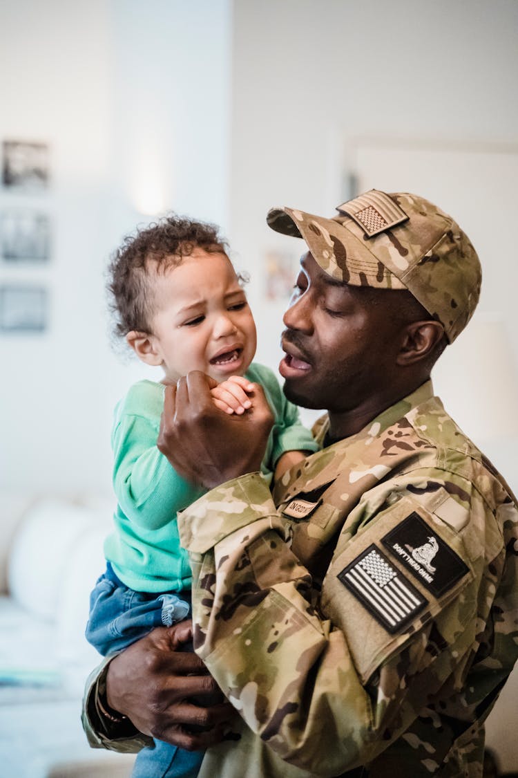 A Man In Uniform Carrying A Crying Baby