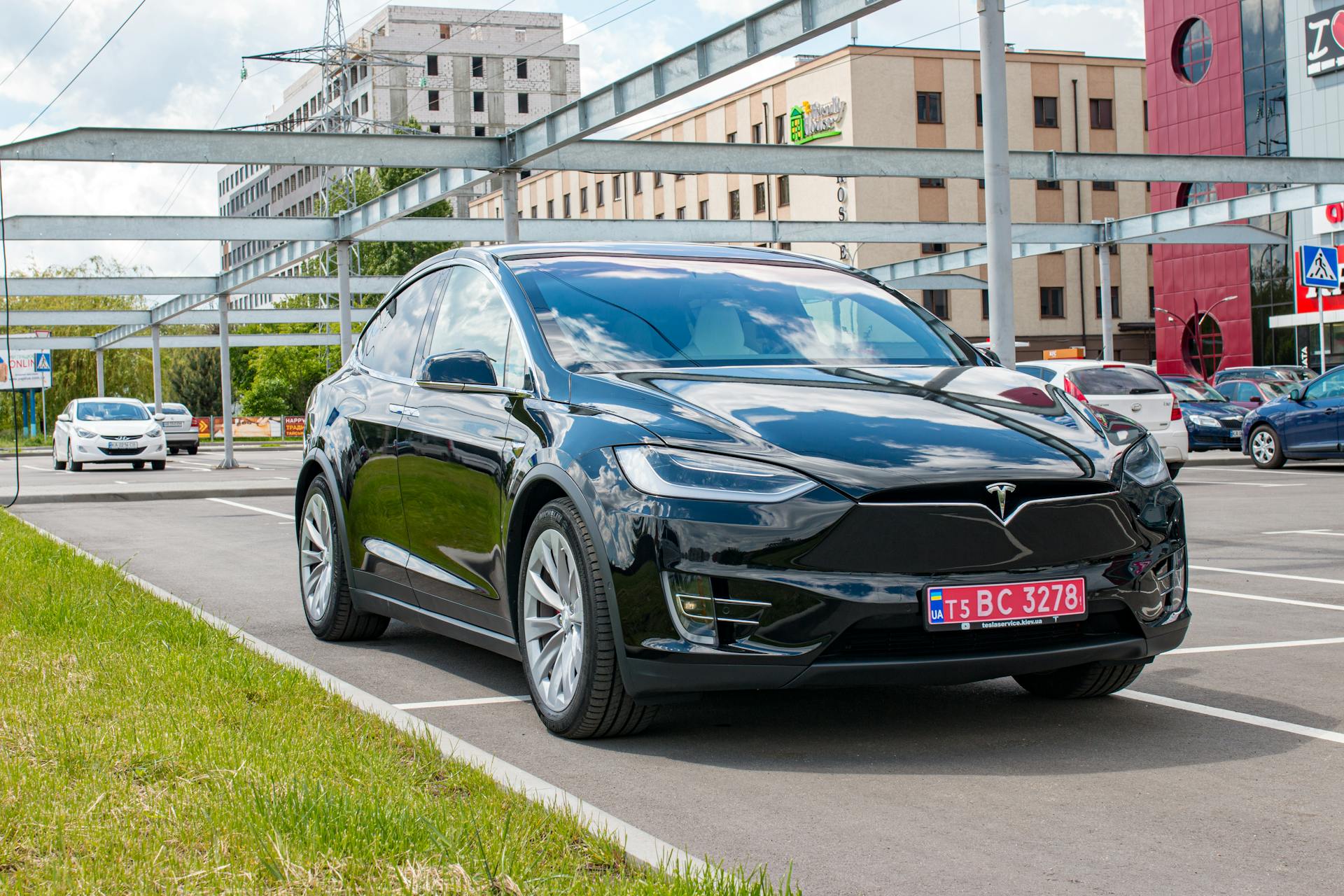 Black Tesla Model X parked in a city lot reflecting buildings with a cloudy sky.