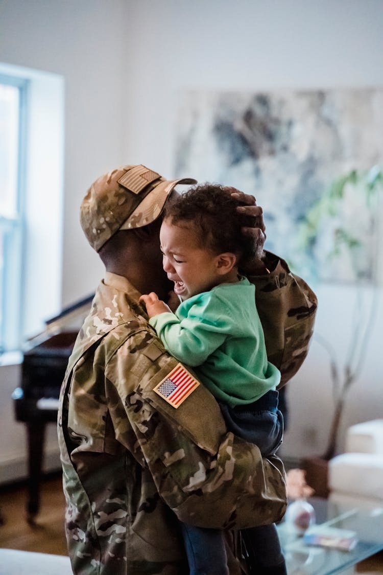 A Person In Military  Uniform Carrying A Crying Child