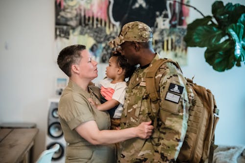 Free A Woman Carrying a Child beside a Man in Military Uniform Stock Photo
