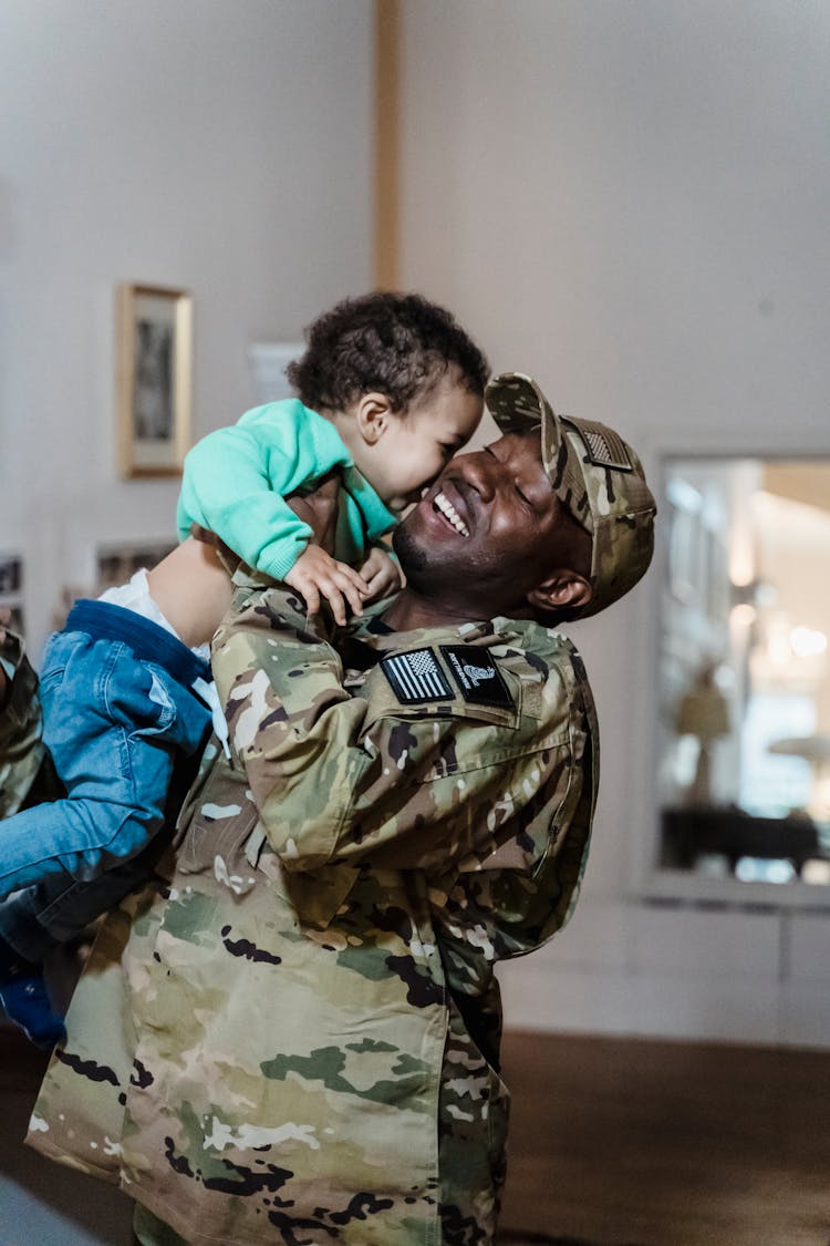 A Man In Military Uniform Carrying A Child Smiling